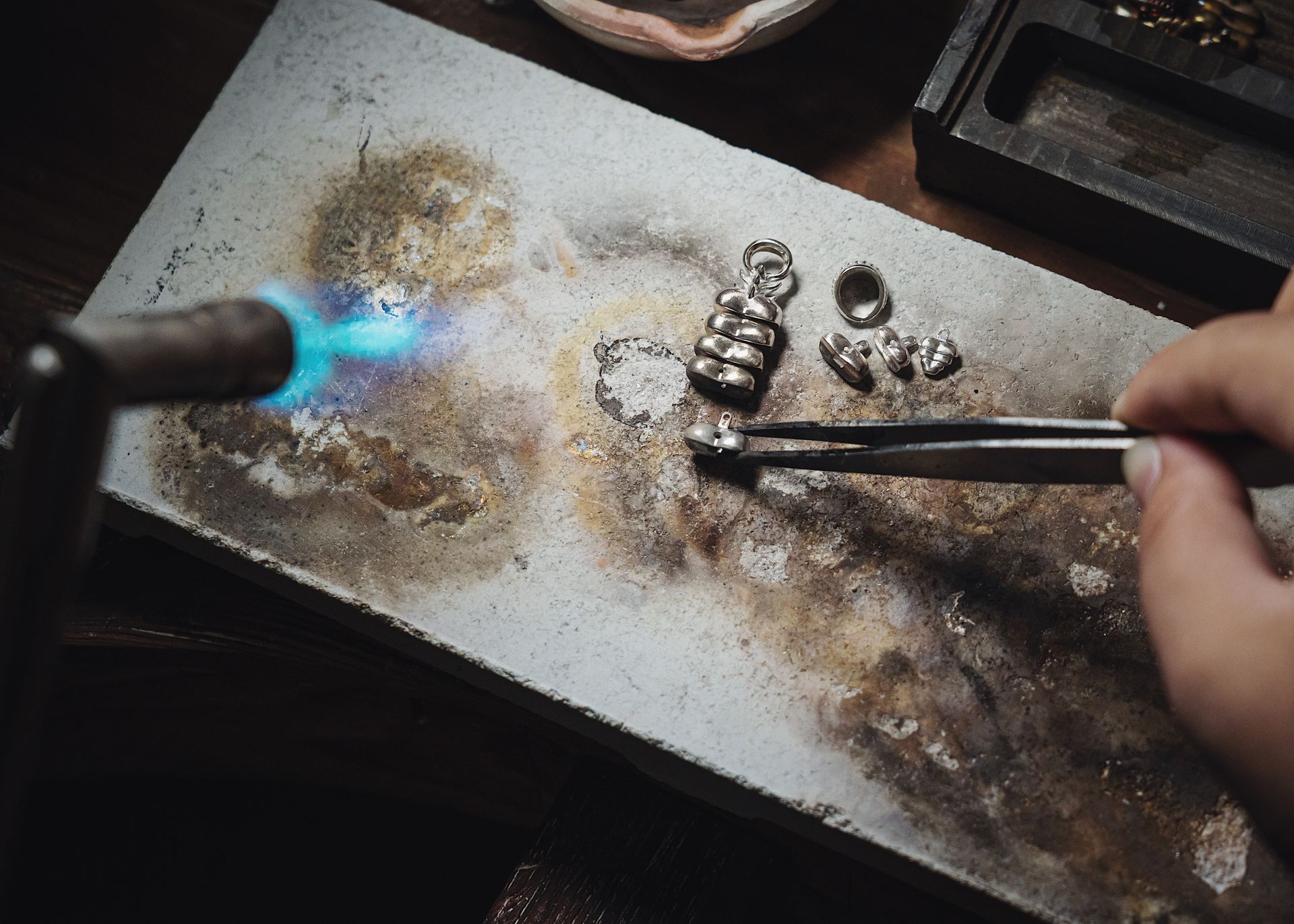 A silversmith soldering a piece of jewellery at a workbench